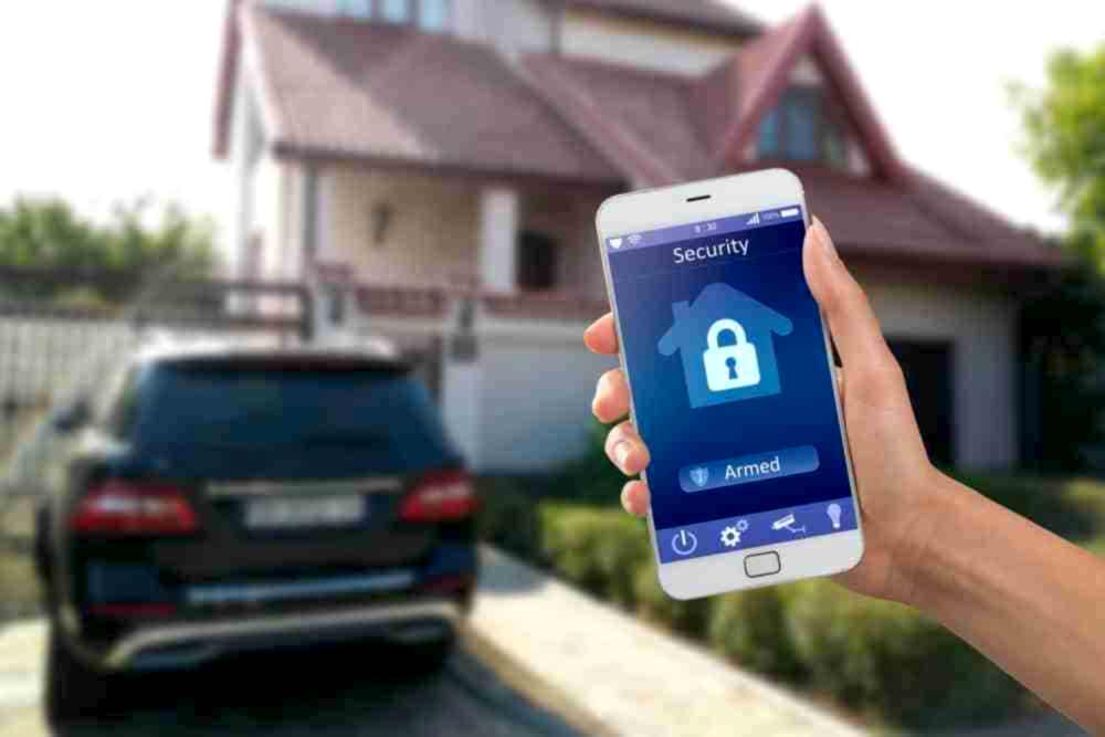 Hand holding a phone with a home security app in front of a house and a parked SUV