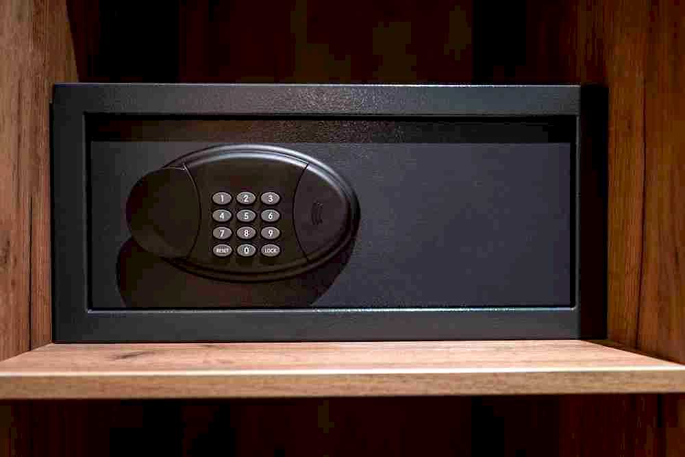 Small black safe with a digital keypad sitting on a wooden closet shelf