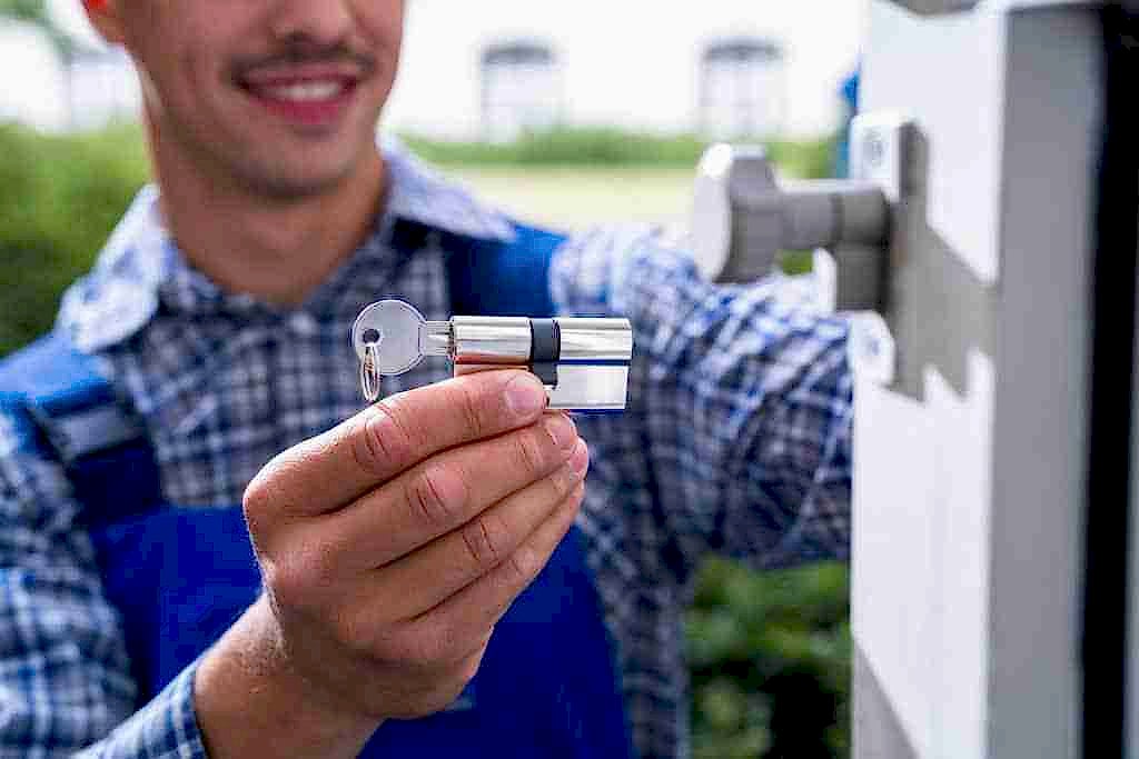 Locksmith holding a new lock cylinder and keys beside a front door